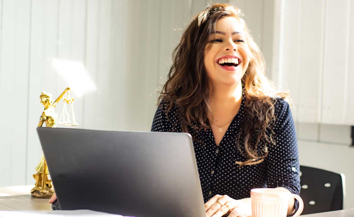 Woman laughing while sitting at table working on laptop.