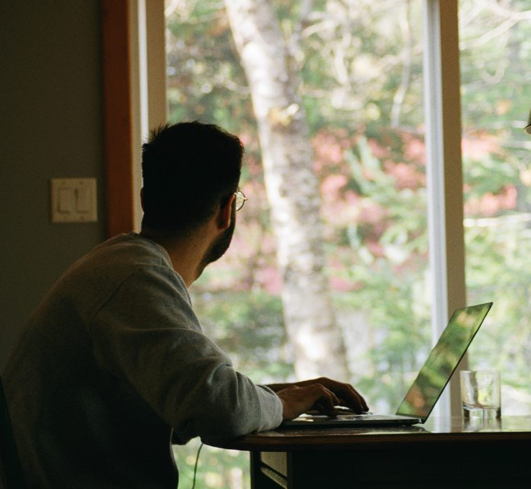 man sits at his desk on his computer while looking out the window