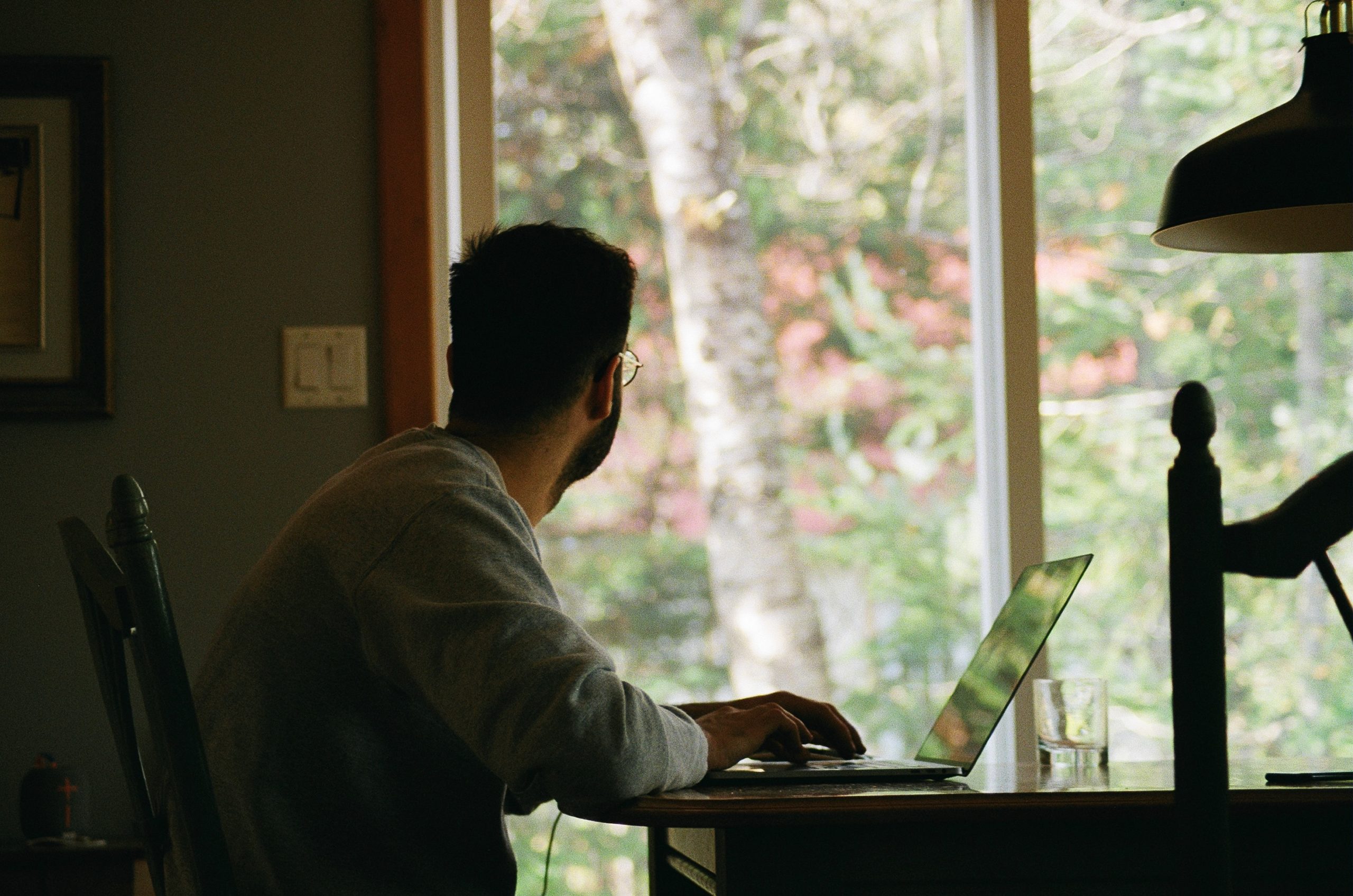 man sits at his desk on his computer while looking out the window